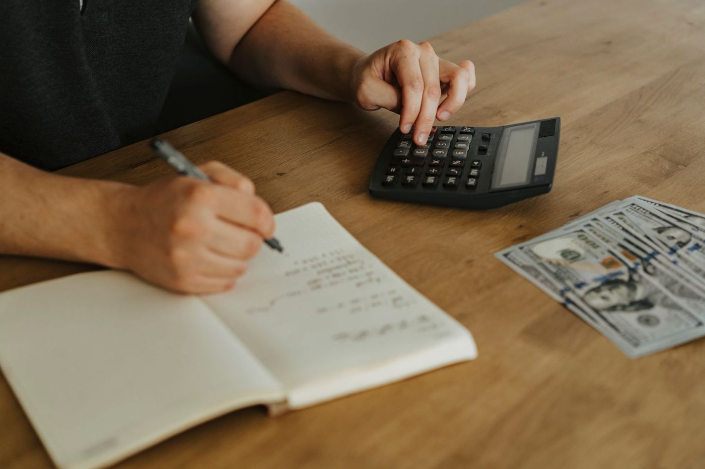Manos anotando cuentas en una libreta junto a una calculadora sobre una mesa de madera