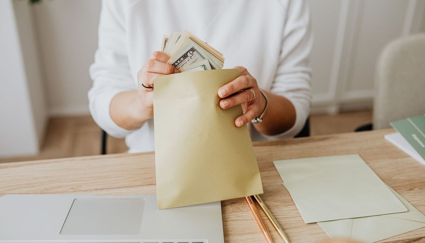 Manos de una mujer guardando billetes en un sobre de papel